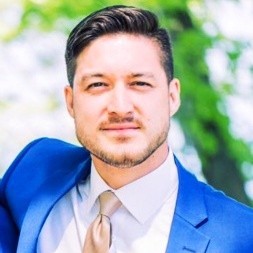Image of a man smiling in a blue suit with trees in the background