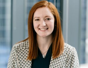 Woman smiling for a headshot photo against a city-scape background