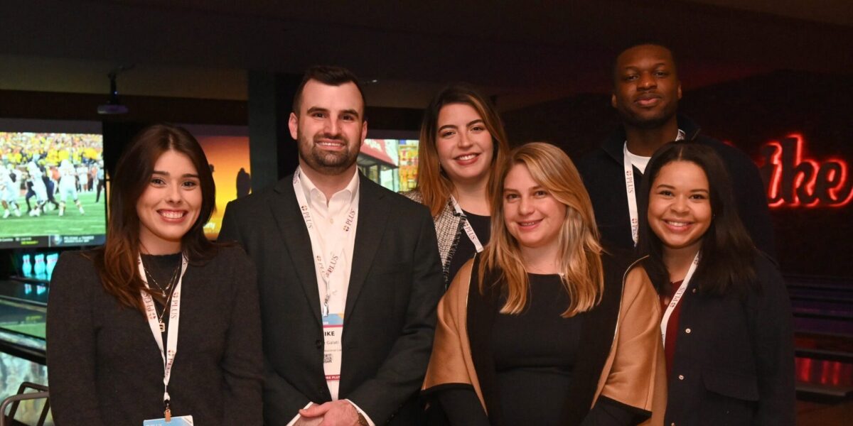 A group of Future PLUS volunteers standing in front of bowling lanes smiling at the 2024 PLUS Conference.