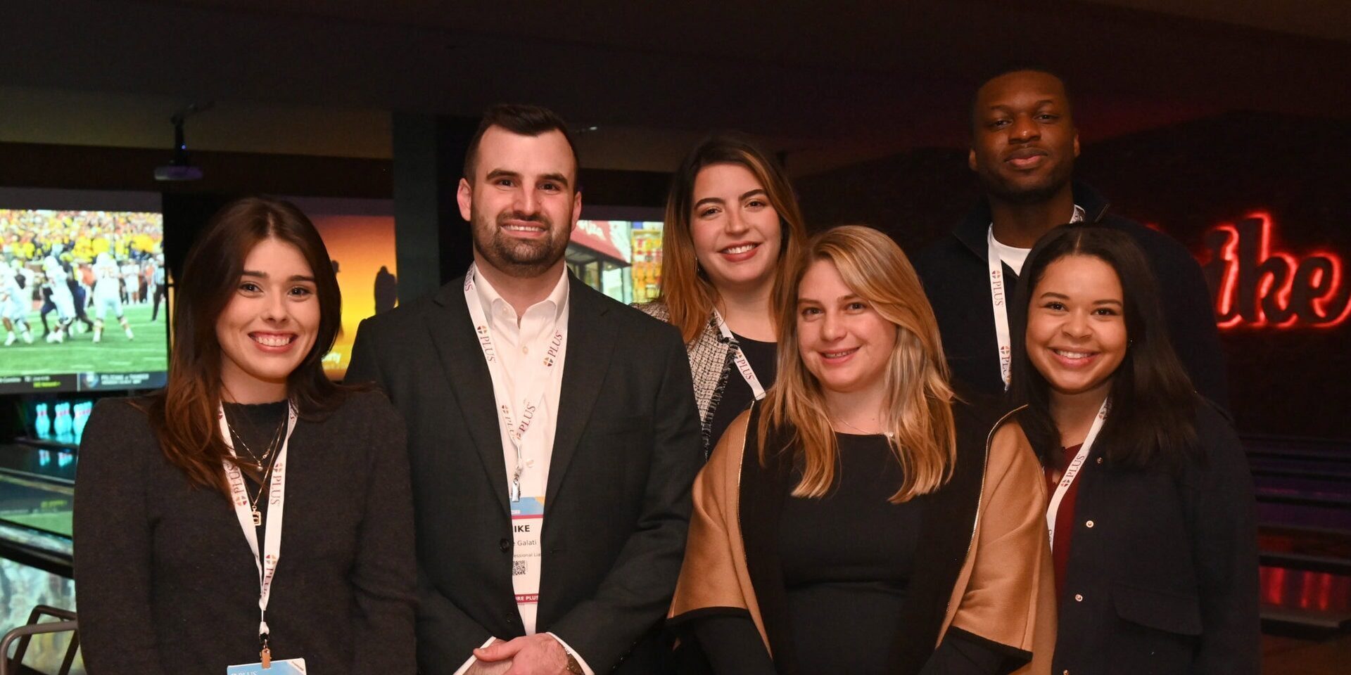 A group of Future PLUS volunteers standing in front of bowling lanes smiling at the 2024 PLUS Conference.