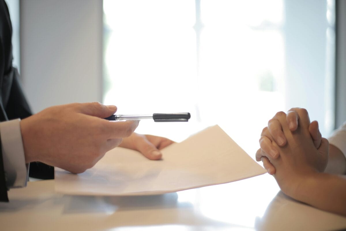 Image of individual offering a pen and contract across the table.