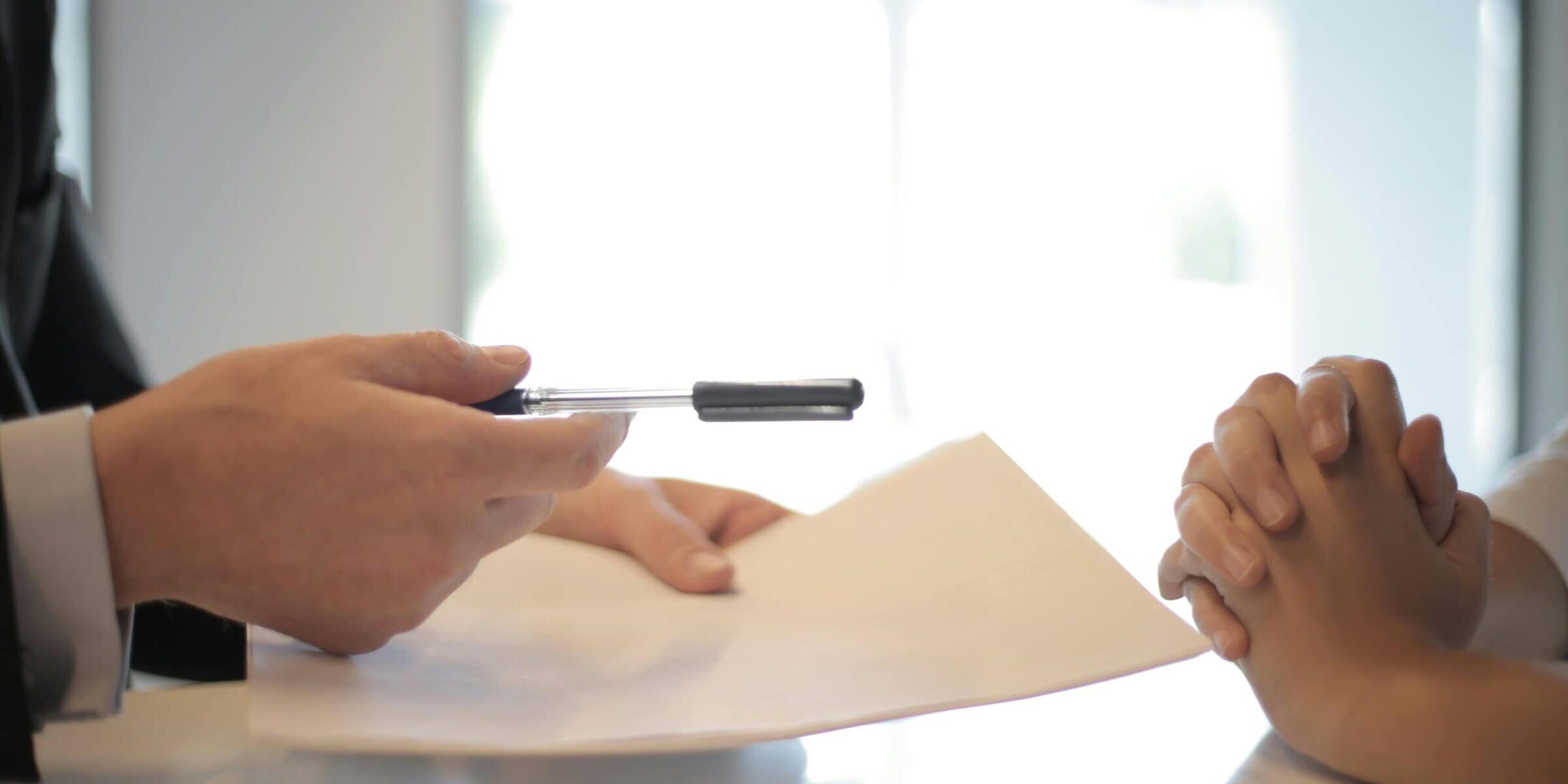 Image of individual offering a pen and contract across the table.