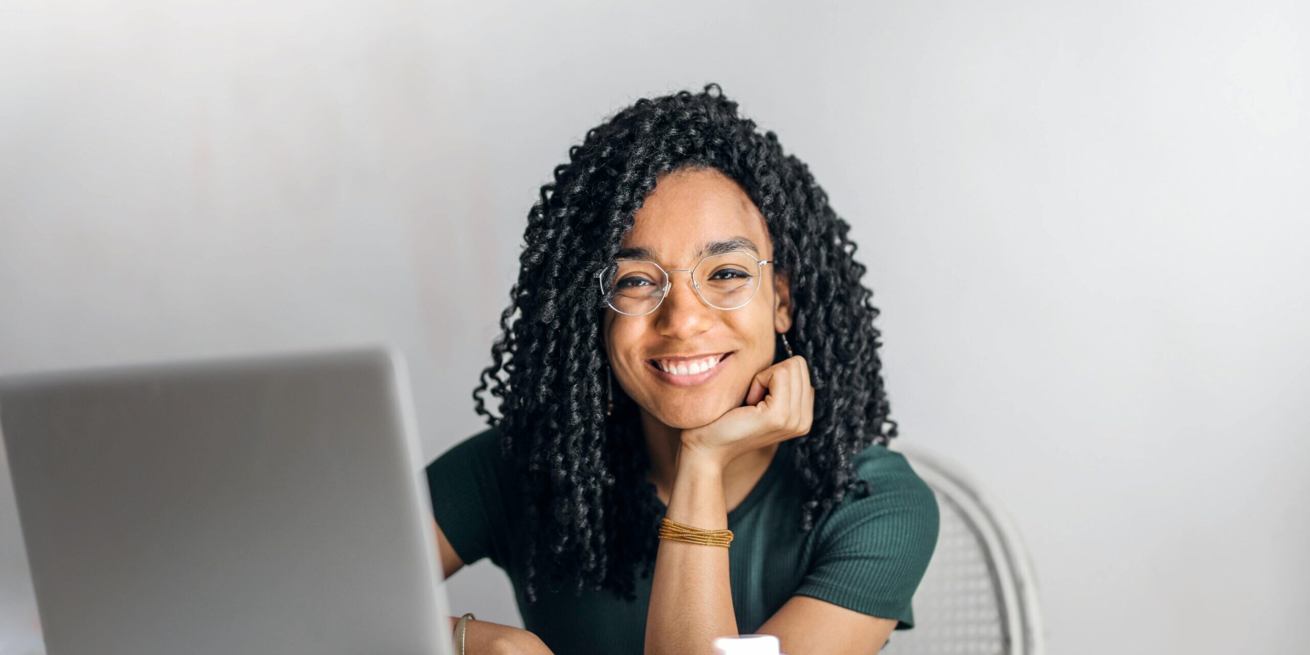 Woman sitting at a desk in front of a laptop, smiling at the camera.