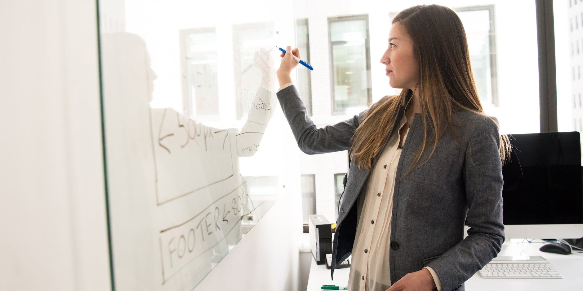 woman wearing gray blazer writing on dry erase board