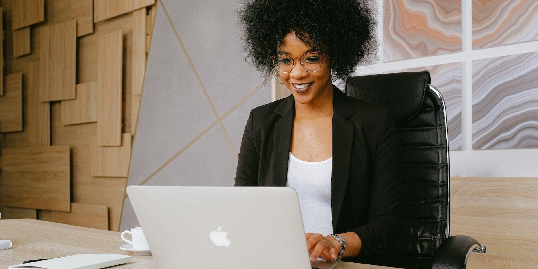 woman in black blazer sitting by the table while using macbook