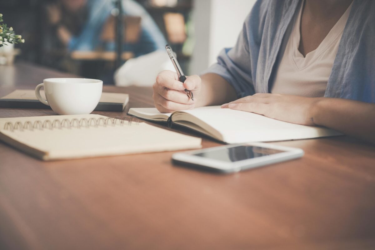 Image of person writing in a notebook on a desk.