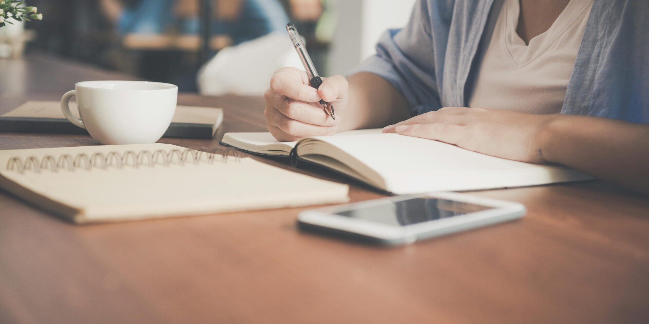 Image of person writing in a notebook on a desk.