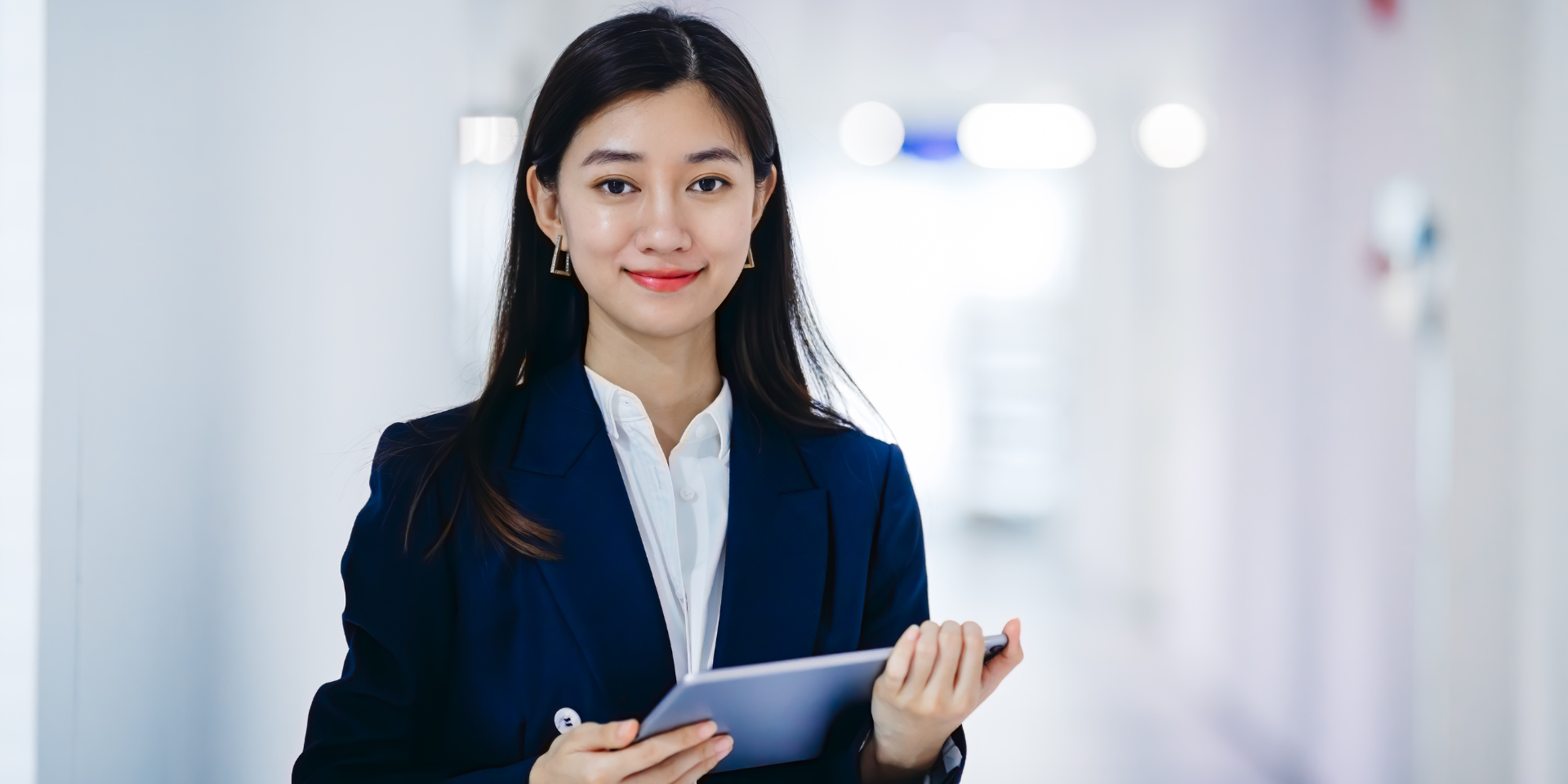 Woman standing holding a tablet in front of a white background.