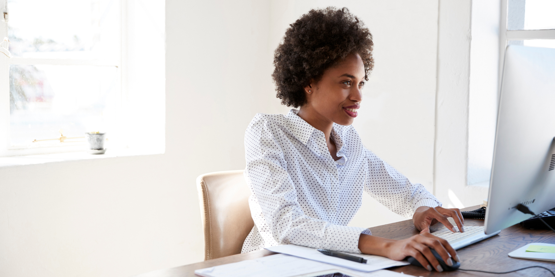 Woman smiling and facing a computer screen. Bright white background behind her.