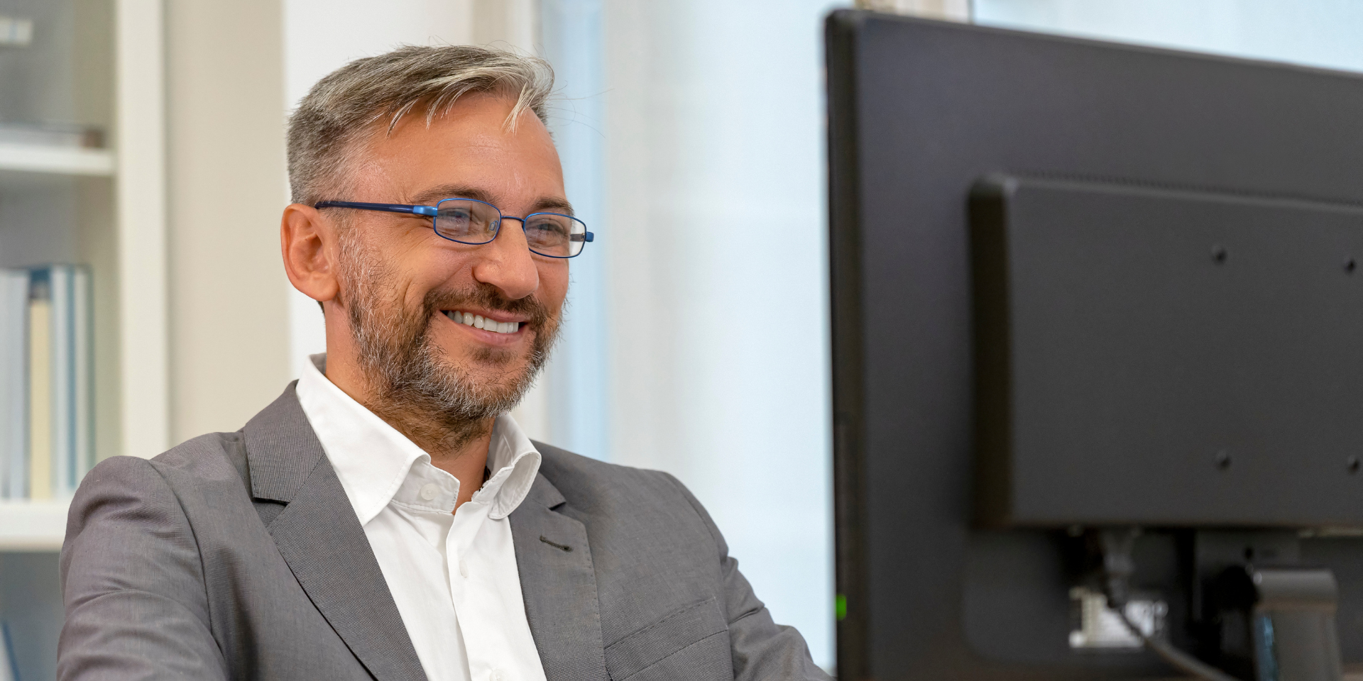 Close up of a man sitting at a desk top computer and smiling.