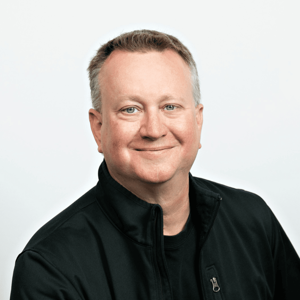 Headshot of Dan Jenney from the shoulders up, smiling, in a black jacket with short brown hair