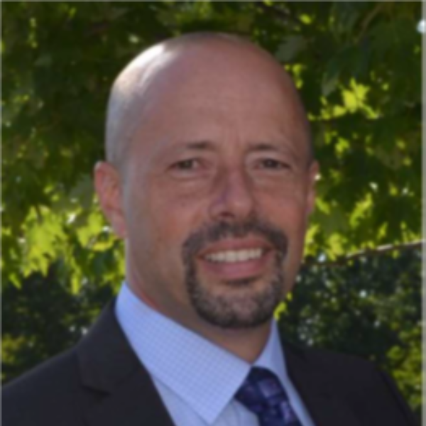 Headshot of Jeff McDonald. Wearing a suit and tie with an outdoorsy background.