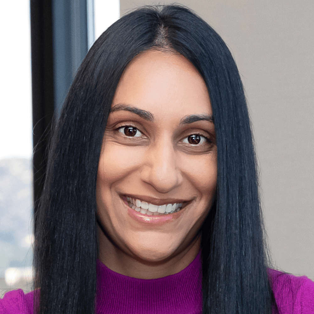 Headshot of Nicole Sheth, from the shoulders up, smiling, in a pink shirt with long black straight hair