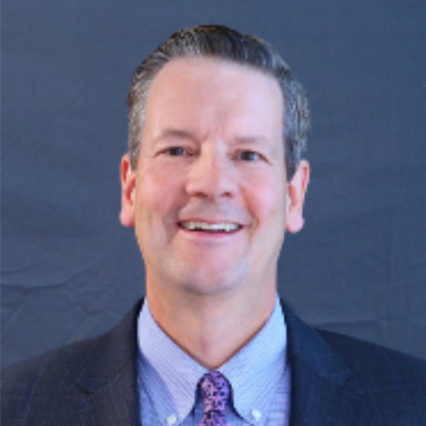 Headshot of Phil Norton. Wearing a suit and tie and smiling from the chest up