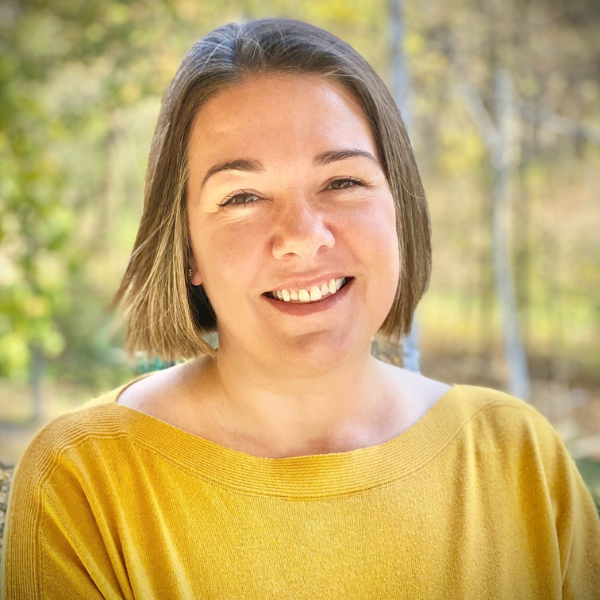 Headshot of Erin Singmaster. She is wearing a yellow shirt with an outdoorsy background