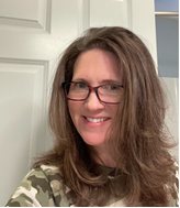 A woman wearing glasses smiling in front of a white door