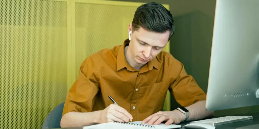 Man sitting in front of computer writing in notebook