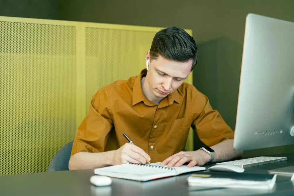 Man sitting in front of computer writing in notebook